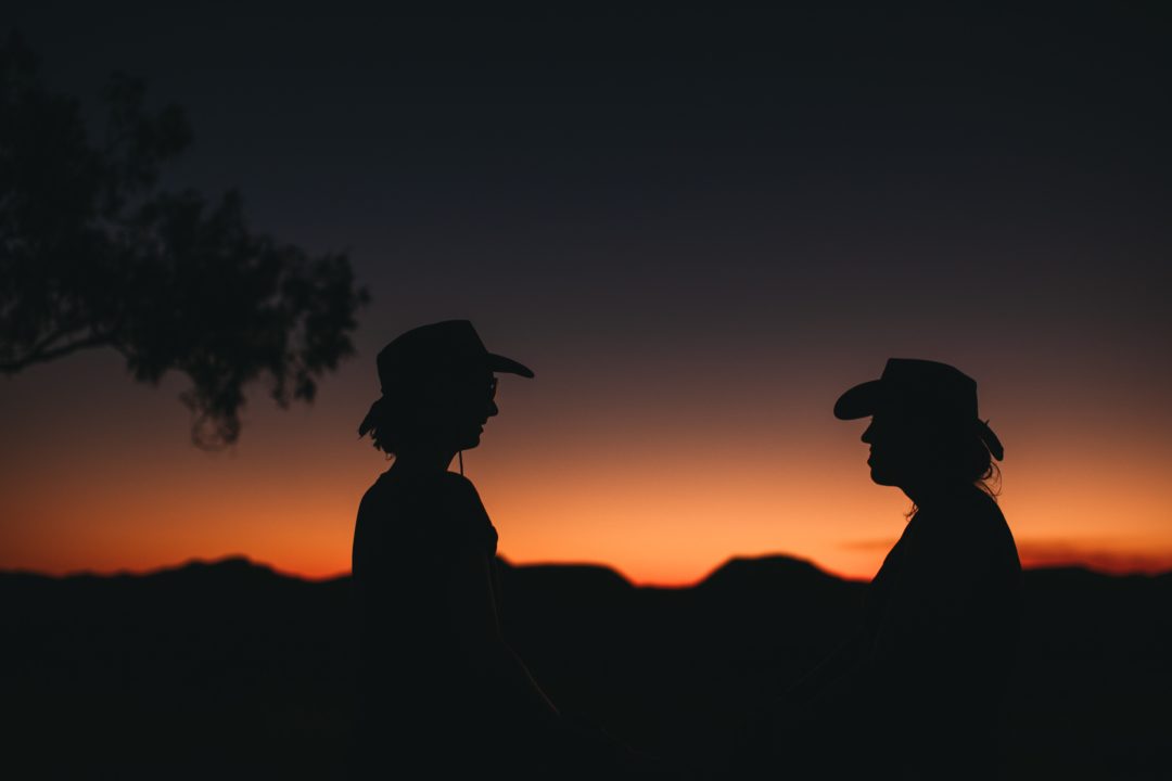 silhouettes of two people in cowboy hats at sunset
