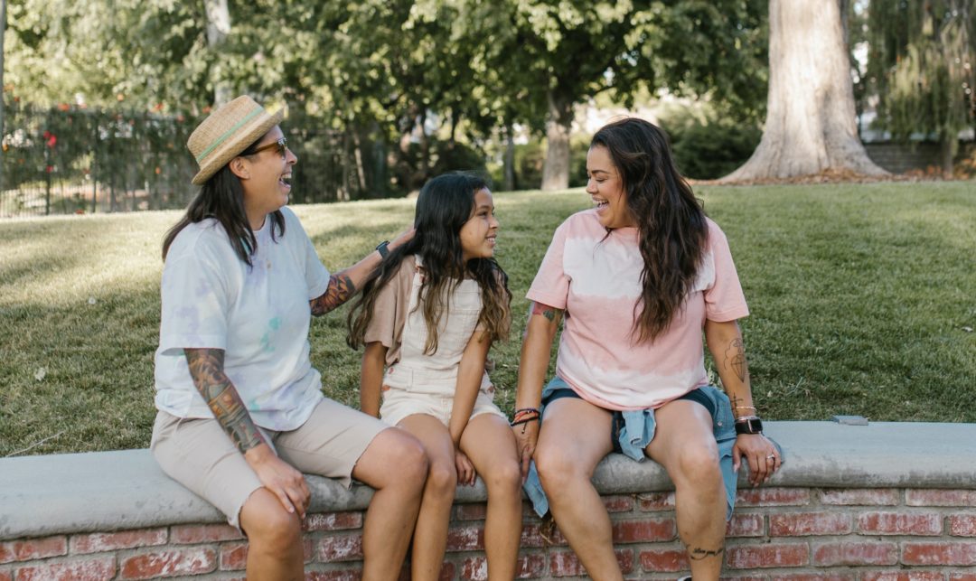 two moms and daughter talking together in a park