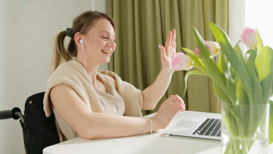 Woman in wheelchair waving to video call on computer