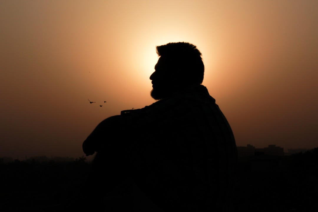 Silhouette of man sitting by sunset