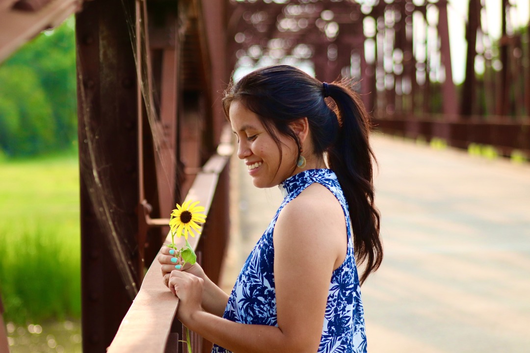 Woman smiling on a bridge holding a sunflower