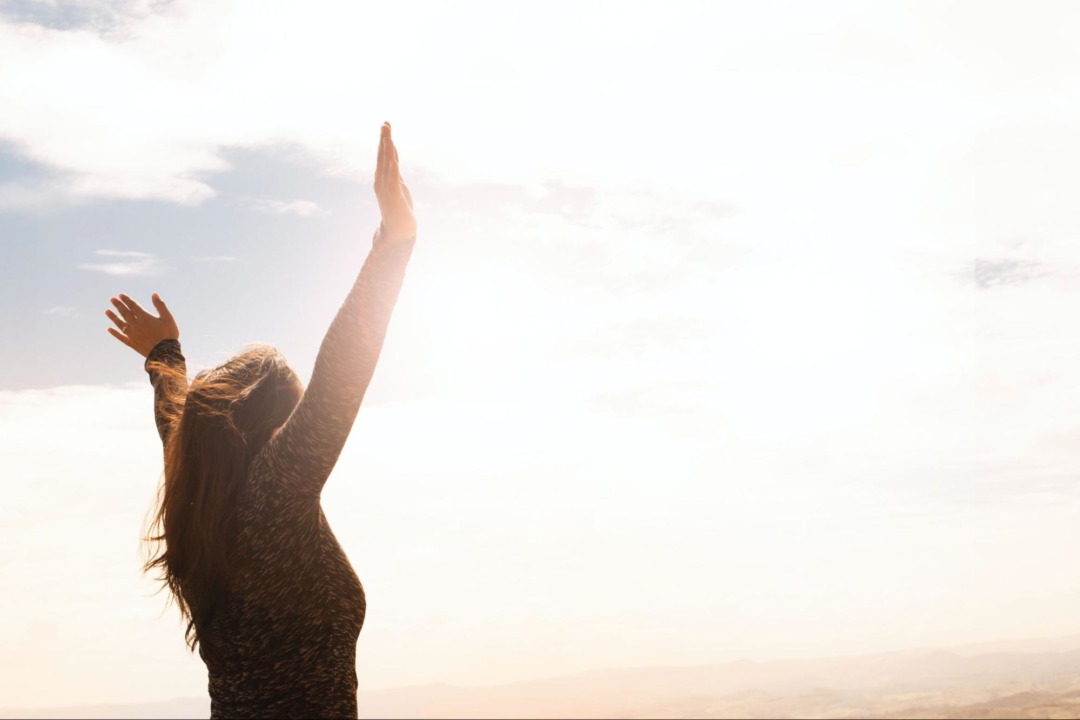 woman with her hands in the air towards the sun and sky