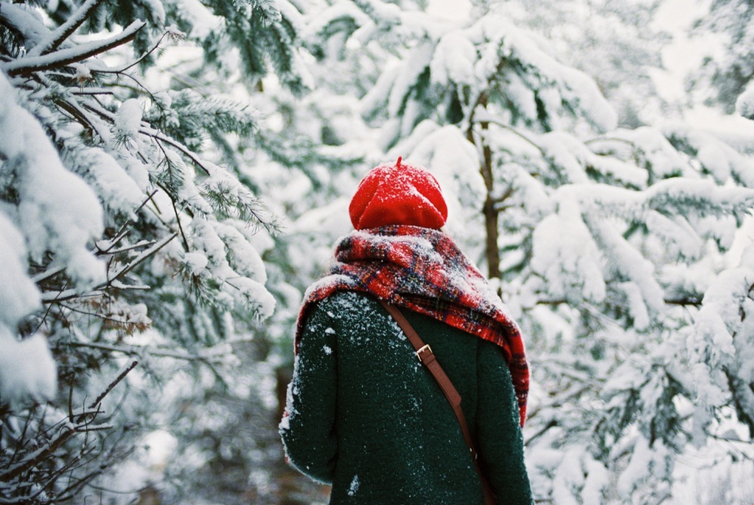 Person walking in the snowy woods with a red beret