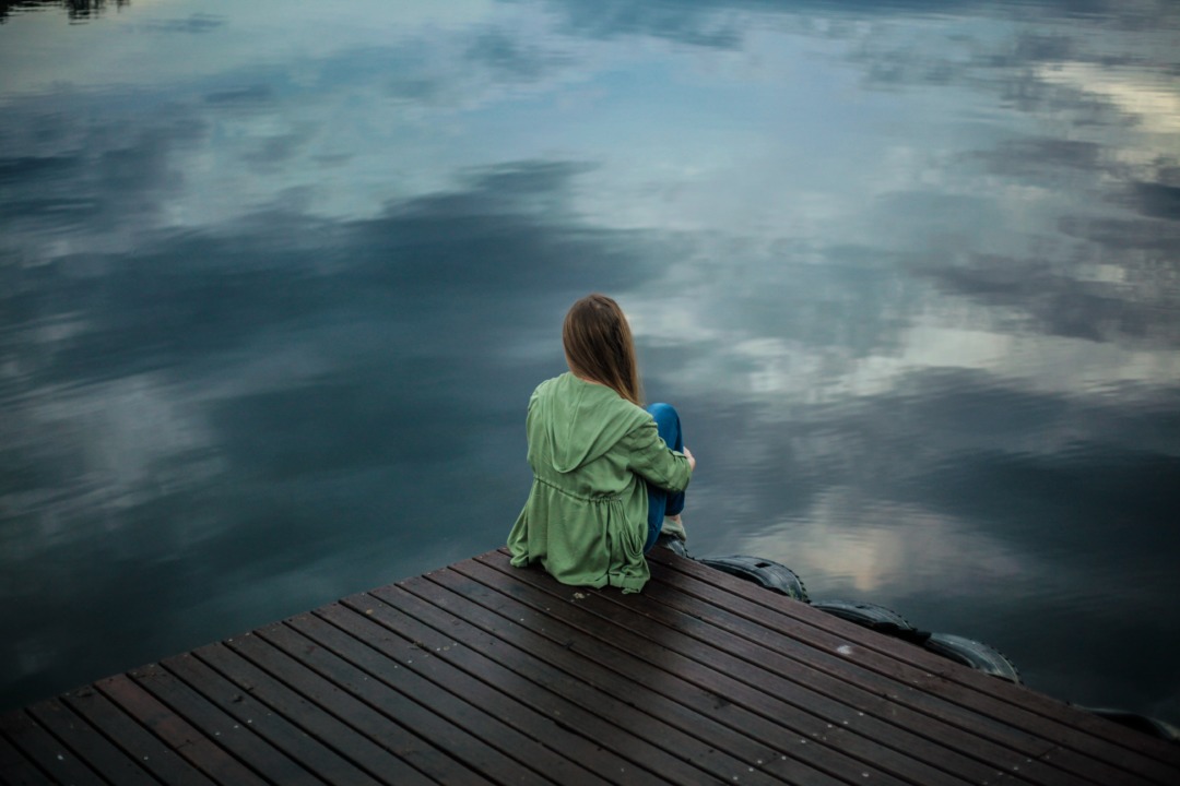 Woman sitting on a dock and looking at the still water