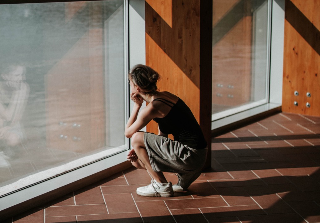 Person squatting and looking out a window