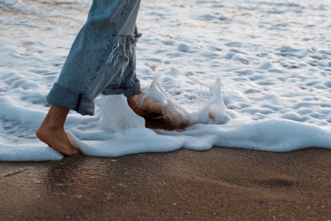 person walking alongside the ocean in ripped jeans