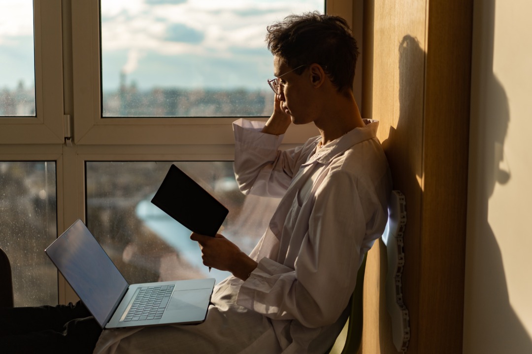 person reading and on computer at a window sill